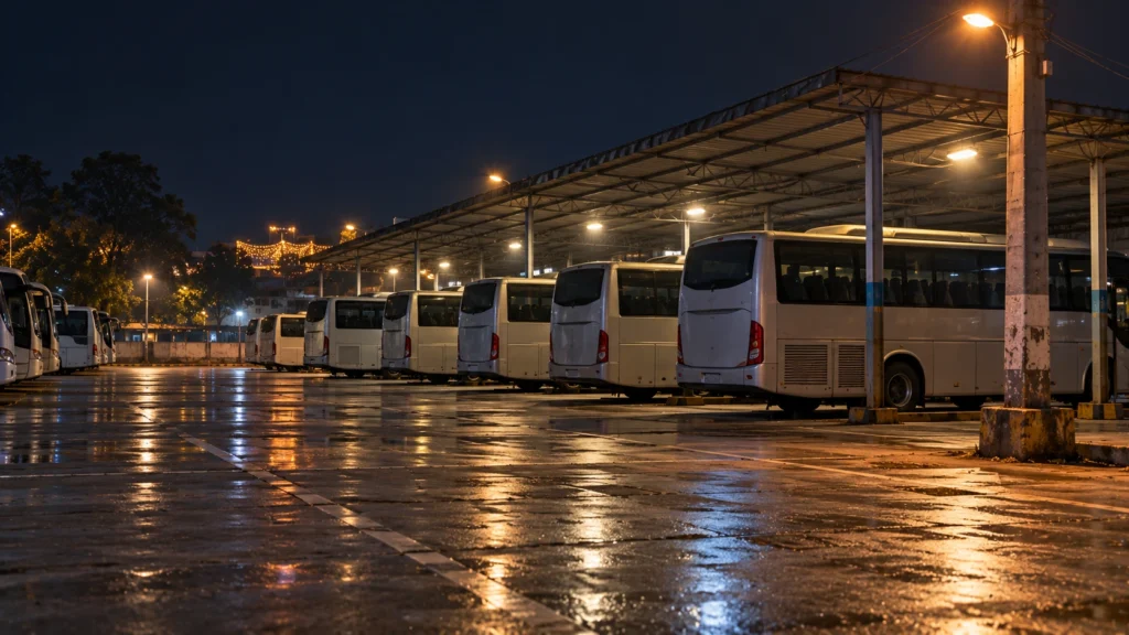 AI-generated editorial illustration of an empty bus stand parking area at night, with plain unmarked parked buses in rows under a bare canopy and an electric pole at the edge; not an incident photograph.